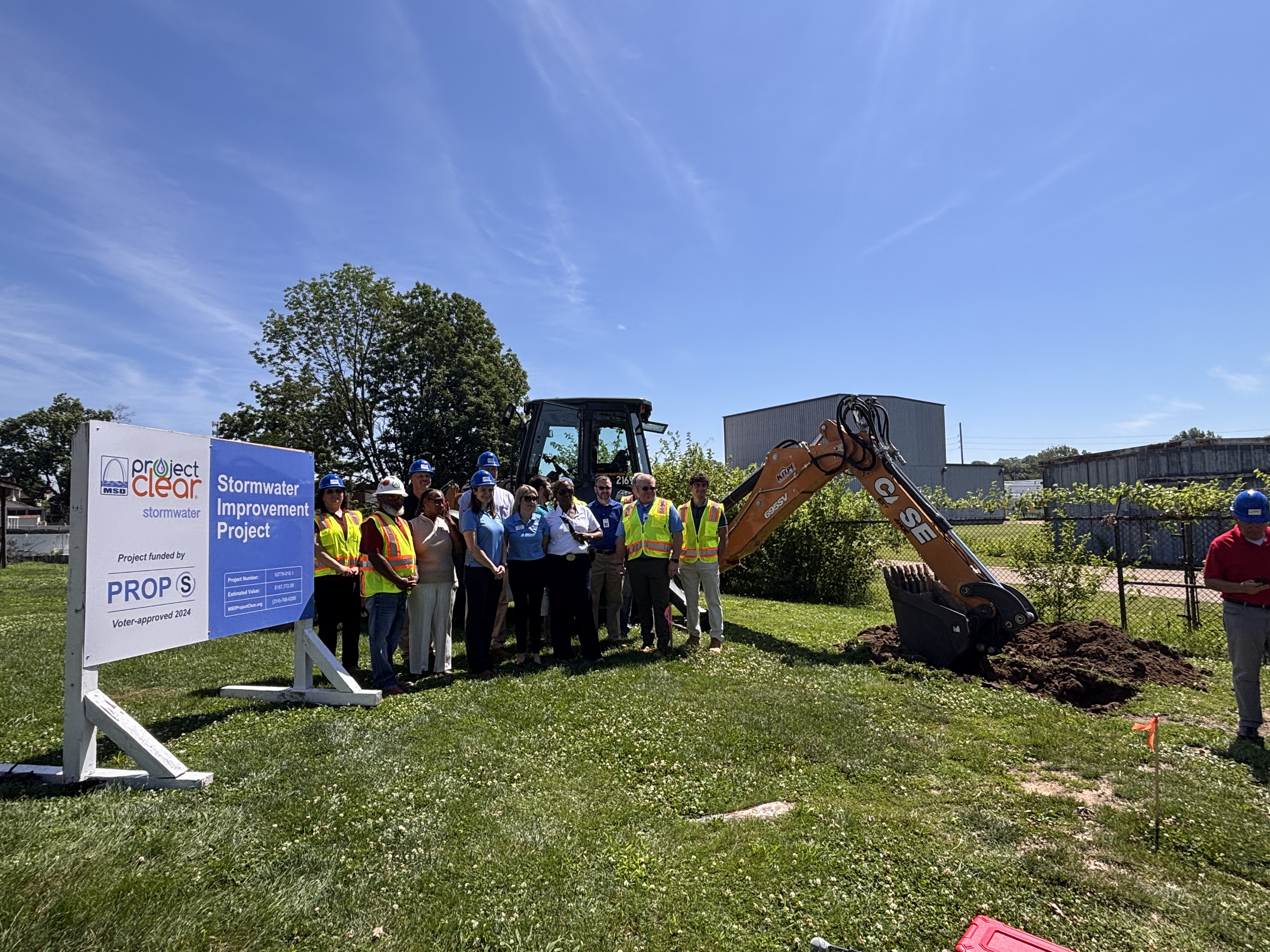 Metropolitan St. Louis Sewer District workers and city leaders in front of site with excavator.