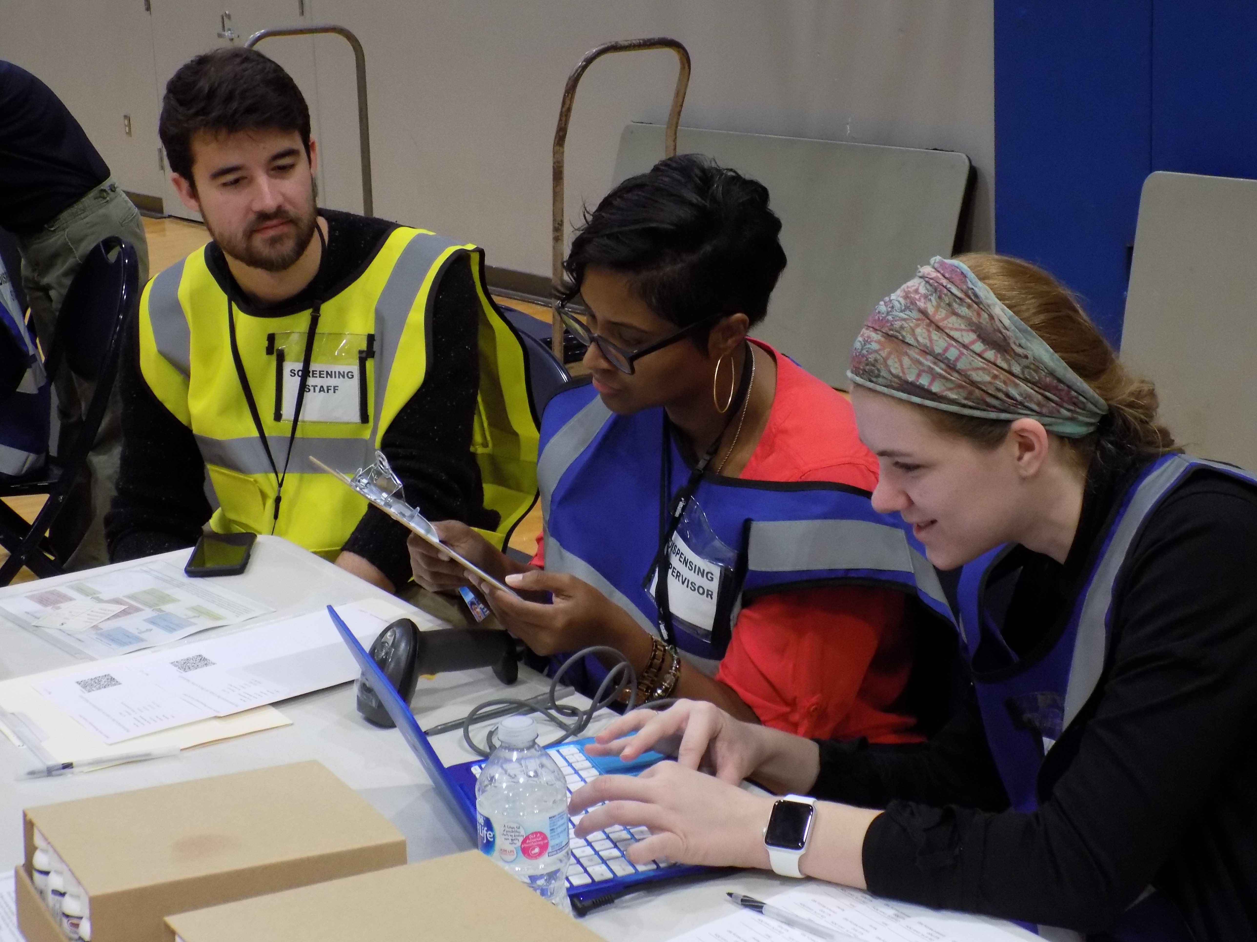 DOH staff and a volunteer review another volunteer's form and dispense medications for the exercise.