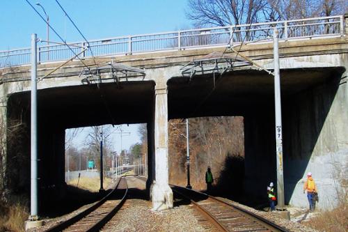 A bridge over railroad tracks. Construction workers work beneath it.